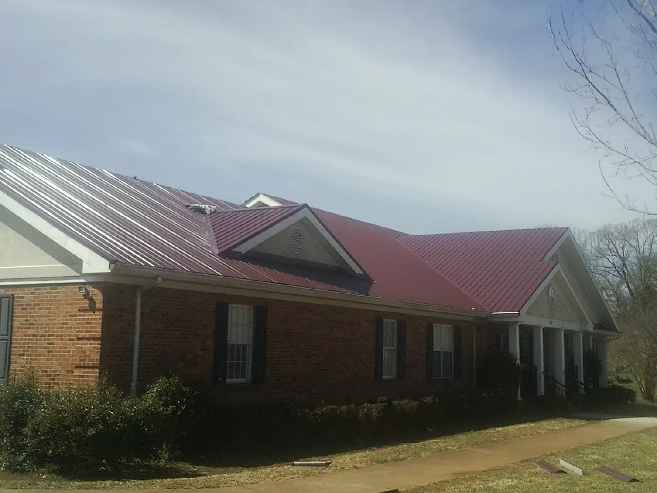 Red metal roof with gabled entries on a long brick building, from a Hail Damage Roof Repair job in West Bloomfield