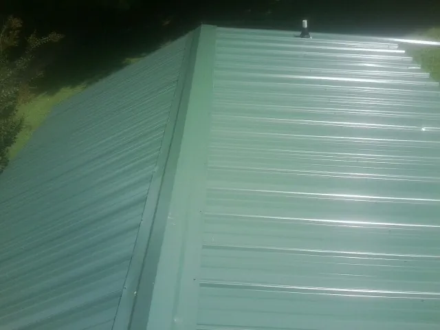New green metal panels meeting at the ridge of a roof — Flat Roof Repair work by our crew in West Bloomfield