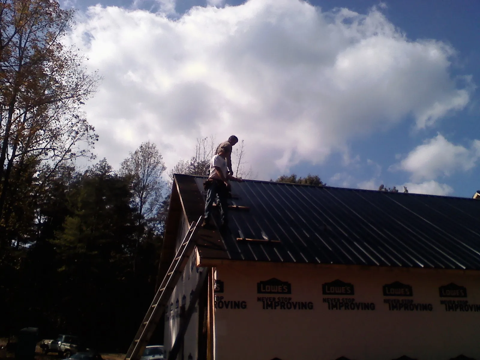 Roofer fastening dark metal panels high against a cloudy sky, from a Roof Inspection job in West Bloomfield