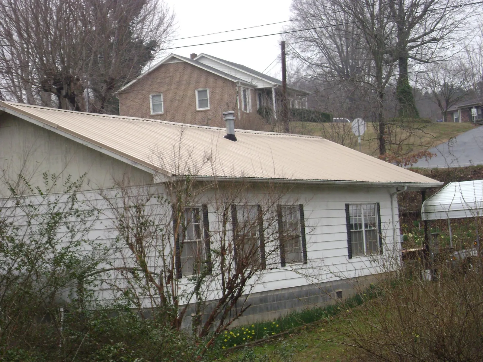 Tan metal roof on a white sided house set into a hillside — Commercial Roofing by Roofing Brothers in West Bloomfield